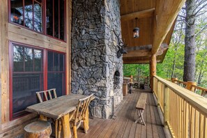 A wooden deck with stone walls, wooden furniture, and a stone fireplace. - Red Stag Lodge at Eagles Nest (Banner Elk)