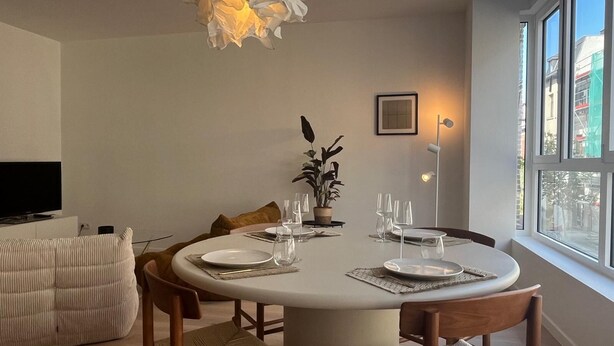 Un coin repas avec une table ronde dressée pour quatre personnes, entourée de chaises en bois.