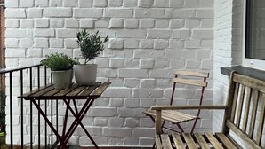 Un petit espace extérieur aménagé avec une table en bois, un banc en bois, deux plantes en pot et un mur en briques blanches.