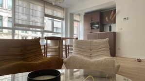 Un salon moderne avec deux canapés, une table basse en verre et une cuisine en arrière-plan.