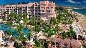 A hotel with a pool, palm trees, and a beach view.