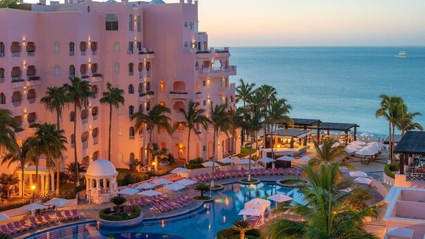 A resort with a large pool, palm trees, and a view of the ocean.