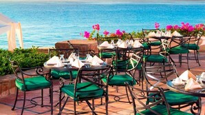 An outdoor dining area with tables and chairs, overlooking a body of water and rocky formations.