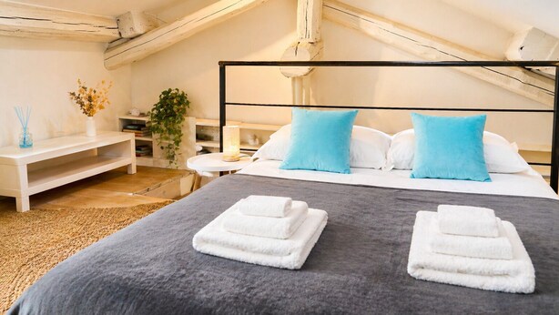 Ein Schlafzimmer mit Bett, Kissen, Nachttisch, Lampe, Pflanze und einem Fenster.