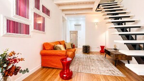 Ein modernes Wohnzimmer mit Treppe, einem Sofa, einer roten Vase und Holzboden.