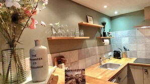 A kitchen with wooden countertops, a sink, and a vase with flowers. There are shelves above the counter holding glasses and a bottle labeled "The Water Co".
