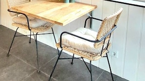 A dining area with a wooden table and wicker chairs, a wall-mounted mirror, and a window with blinds.