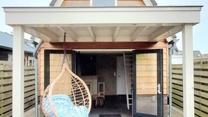 A modern house with a covered porch, a hanging chair, and a small window.