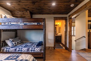 A bunk bed with a quilted bedspread, a wooden ceiling, and a hallway leading to a bathroom with a mirror and towel rack. - The Lookout at Eagles Nest (Banner Elk)