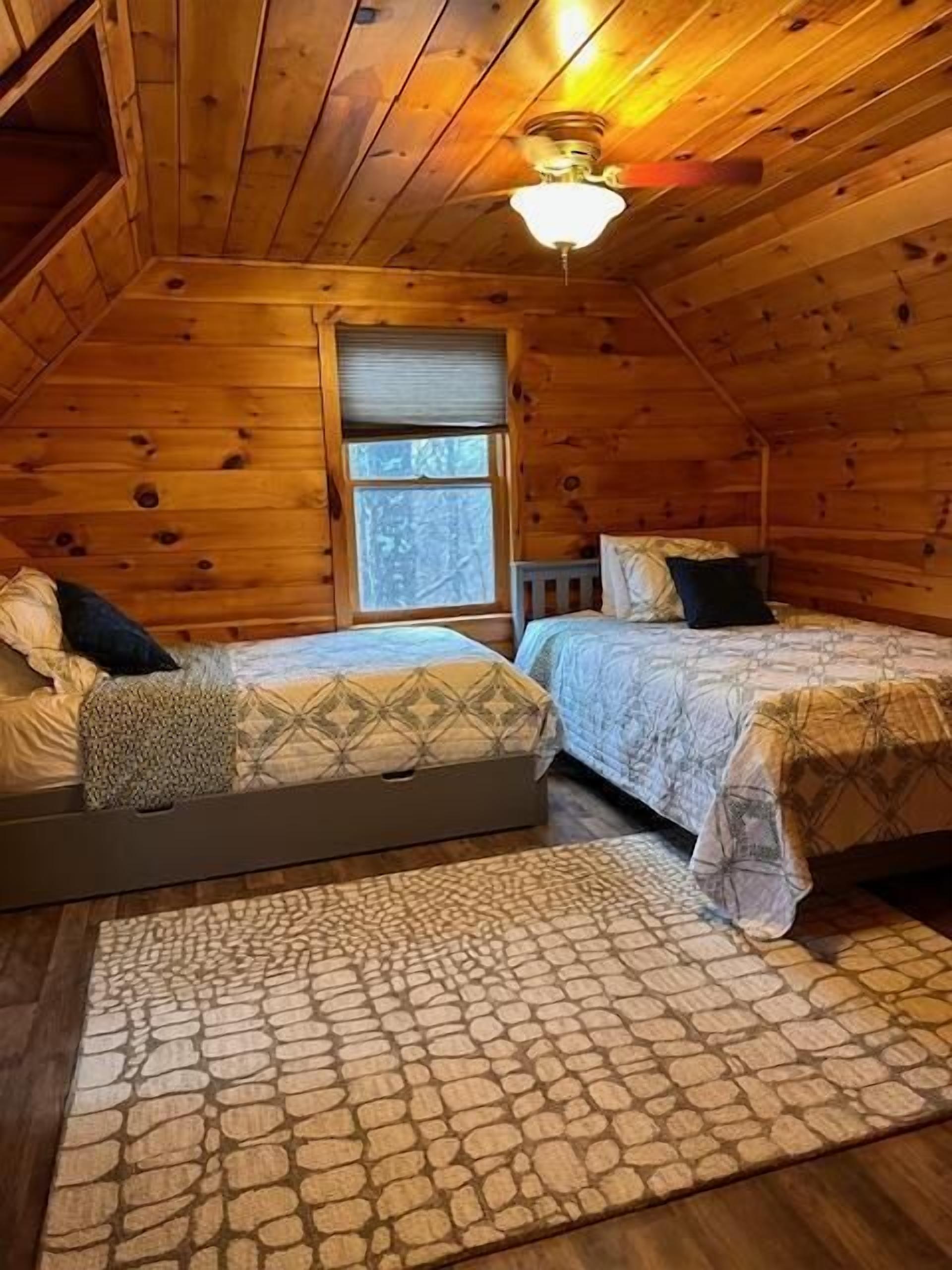 A cozy attic bedroom with two beds, a window, and a ceiling fan.