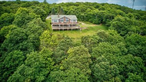 A large house with a deck, surrounded by dense forest. - Shooting Star Lodge (Boone)