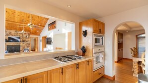 A modern kitchen with wooden cabinets, a stone backsplash, a gas stove, and a microwave. - Shooting Star Lodge (Boone)