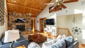 A spacious living room with a stone fireplace, wooden ceiling, and a large TV. - Shooting Star Lodge (Boone)