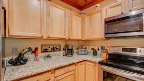 A kitchen with wooden cabinets, granite countertops, a stainless steel microwave, a coffee maker, and a stove. - Kaylee's Kabin (Vilas)