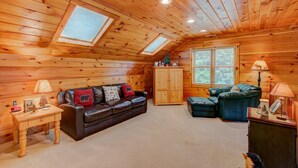 A cozy log cabin interior with a leather sofa, a wooden cabinet, and a window with blinds. - Kaylee's Kabin (Vilas)