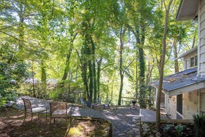 Un espacio al aire libre cubierto con un sendero de piedra, sillas de metal y una terraza de madera.