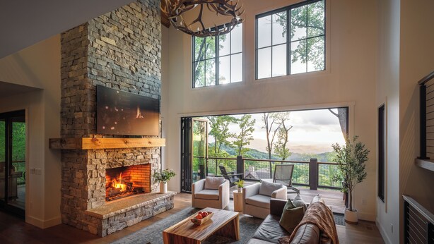 Ein geräumiges Wohnzimmer mit Kamin aus Stein, bequemen Sitzmöglichkeiten und einem großen Fenster mit Blick auf eine reizvolle Landschaft.