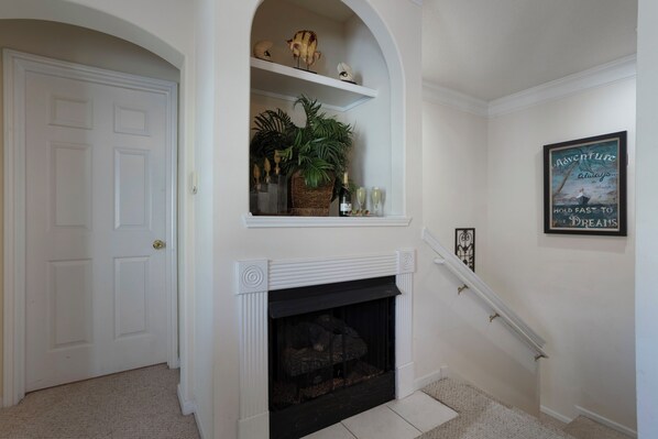 A hallway with a white door, a fireplace with a basket of plants, and a framed poster on the wall.