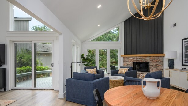 A spacious living area with a fireplace, blue sofas, a wooden dining table, and large windows offering a view of the outdoors. - Close to the Beach! (Hilton Head Island)