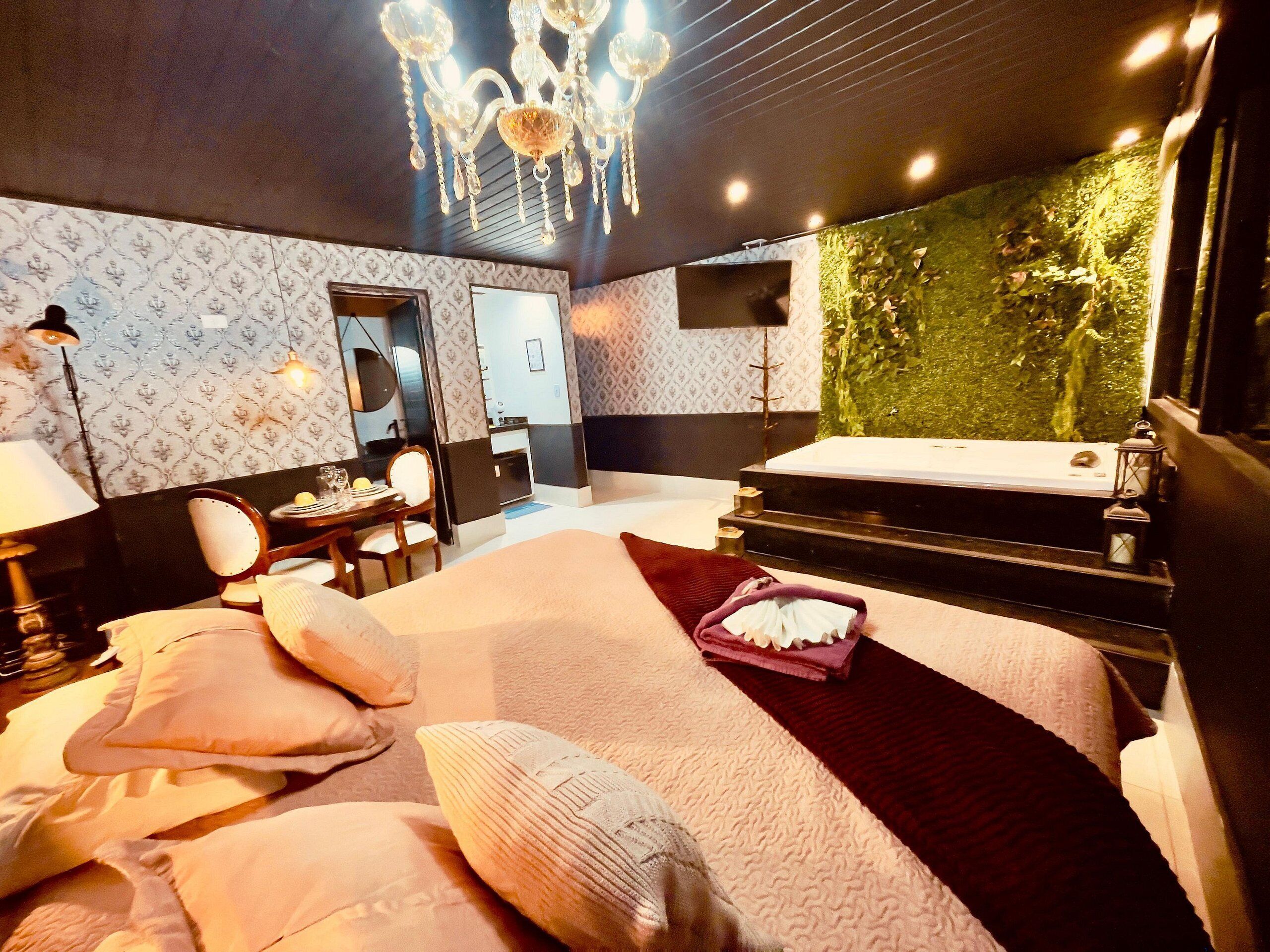 A modern hotel room with a large bed, a desk with a chair, a vanity with a mirror, and a green wall with a waterfall feature.