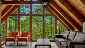 Une pièce mansardée spacieuse, dotée de grandes fenêtres, d’un canapé en cuir, d’une table basse en bois et de deux fauteuils.