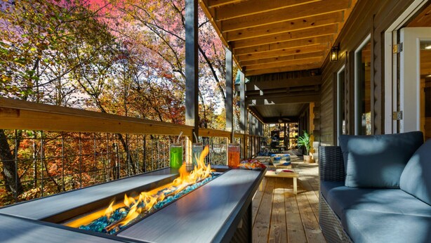 Un espace extérieur aménagé, abrité et doté d’un foyer, offrant une vue sur les arbres aux couleurs automnales.