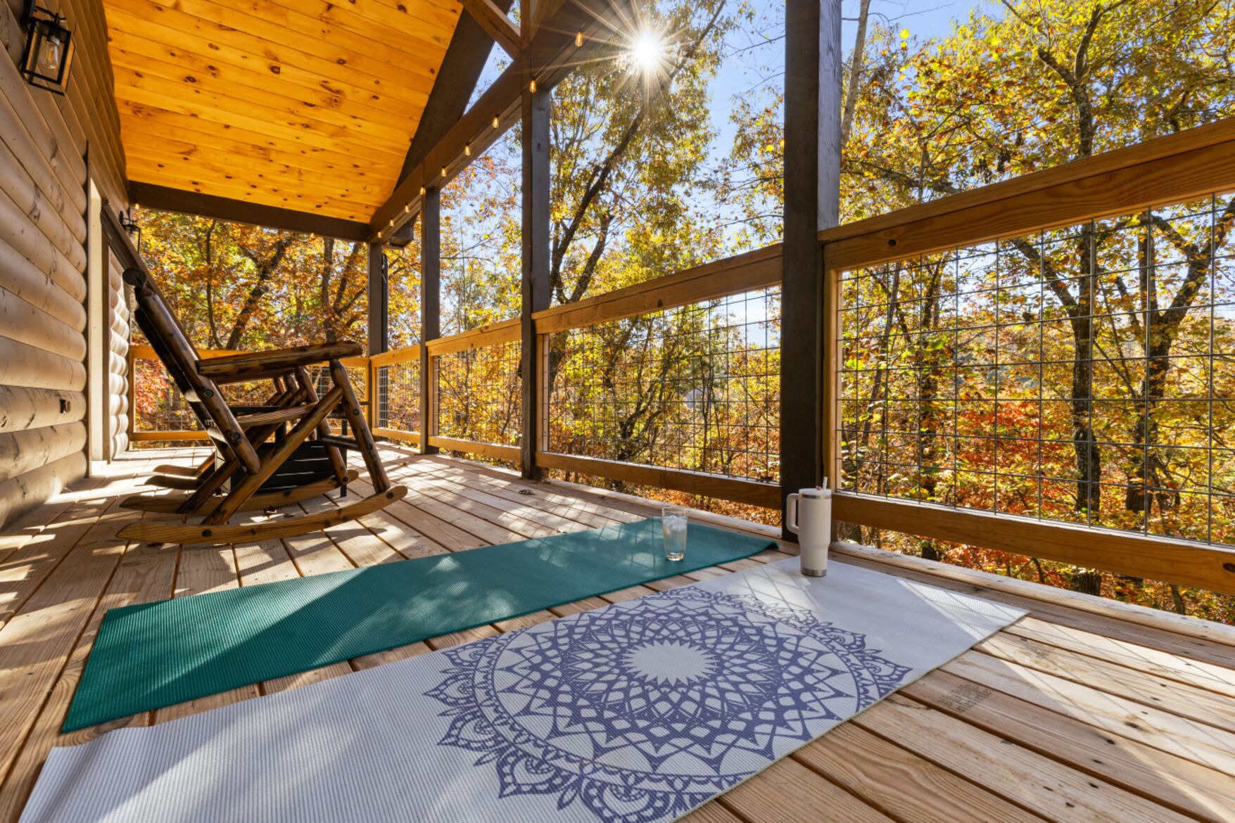 Una terraza de madera con una mecedora, un tapete de meditación y vistas a árboles otoñales.