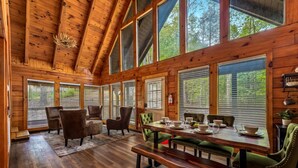 L’intérieur d’un chalet en bois comprend un coin repas, de nombreuses fenêtres et une cheminée.
