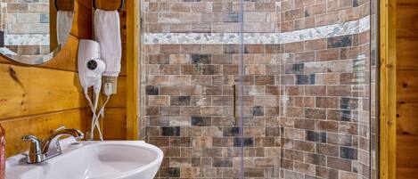 Un baño con un lavamanos blanco, un secador de pelo y una ducha con pared de mosaicos.