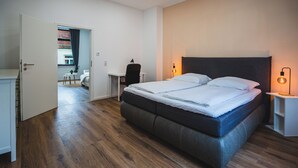 Une chambre moderne avec un grand lit, un plancher en bois, un bureau et une chaise.