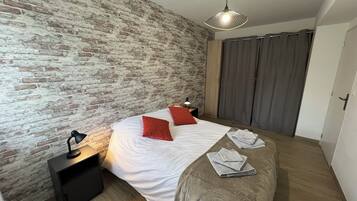 Une chambre avec un mur en briques, un lit avec une literie blanche et des oreillers rouges, une table de chevet avec une lampe et un luminaire suspendu.
