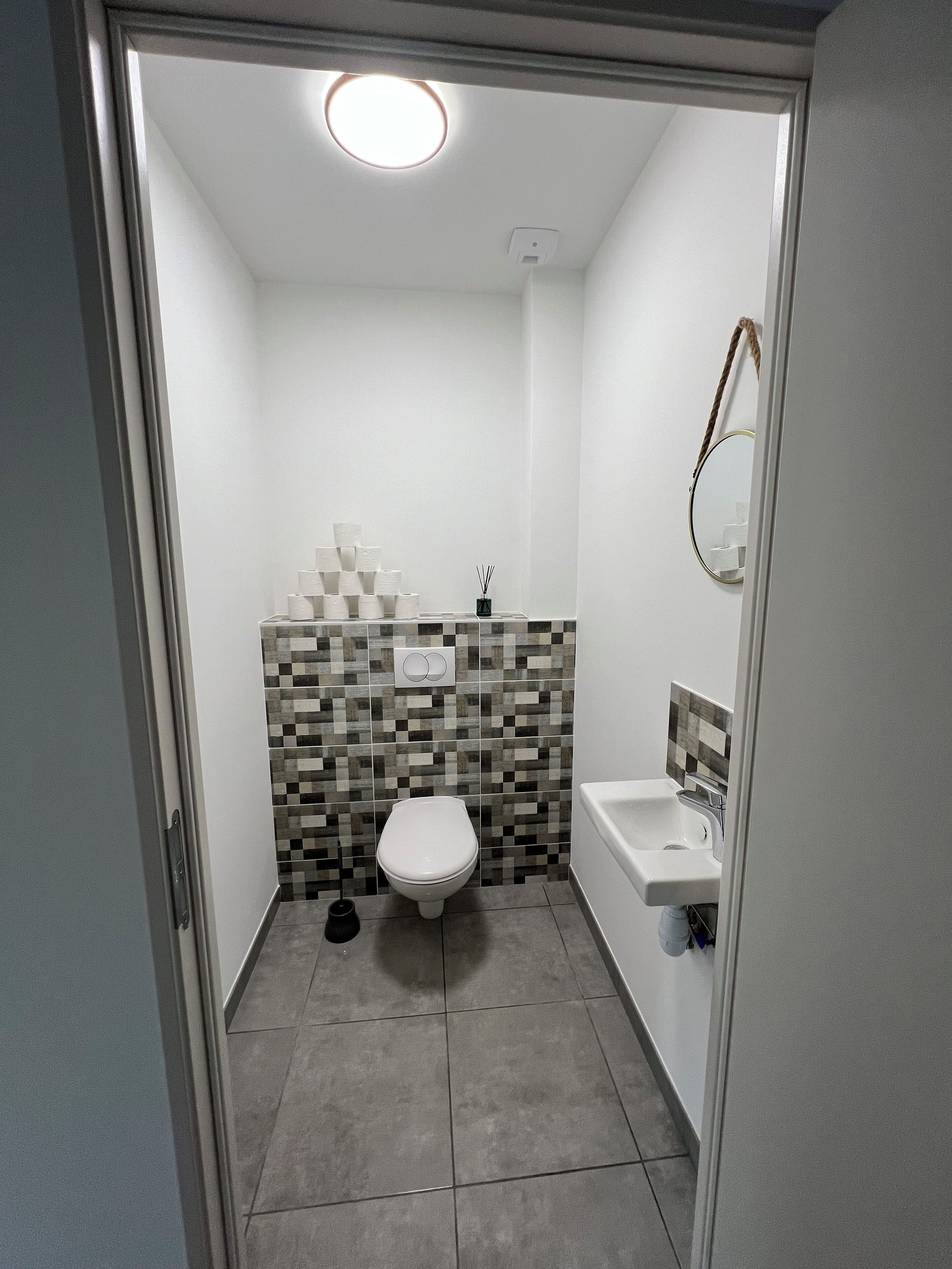 A small, modern bathroom with a toilet, sink, and tiled walls.