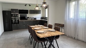 Een moderne keuken met donkere kastjes, een ingebouwde oven en een magnetron. Er staat een eettafel met stoelen en borden klaar voor een maaltijd.