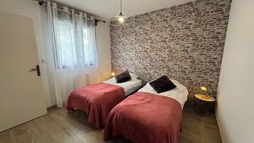 Une chambre avec deux lits, un mur en briques, un plancher en bois, une fenêtre avec des rideaux et un luminaire suspendu.