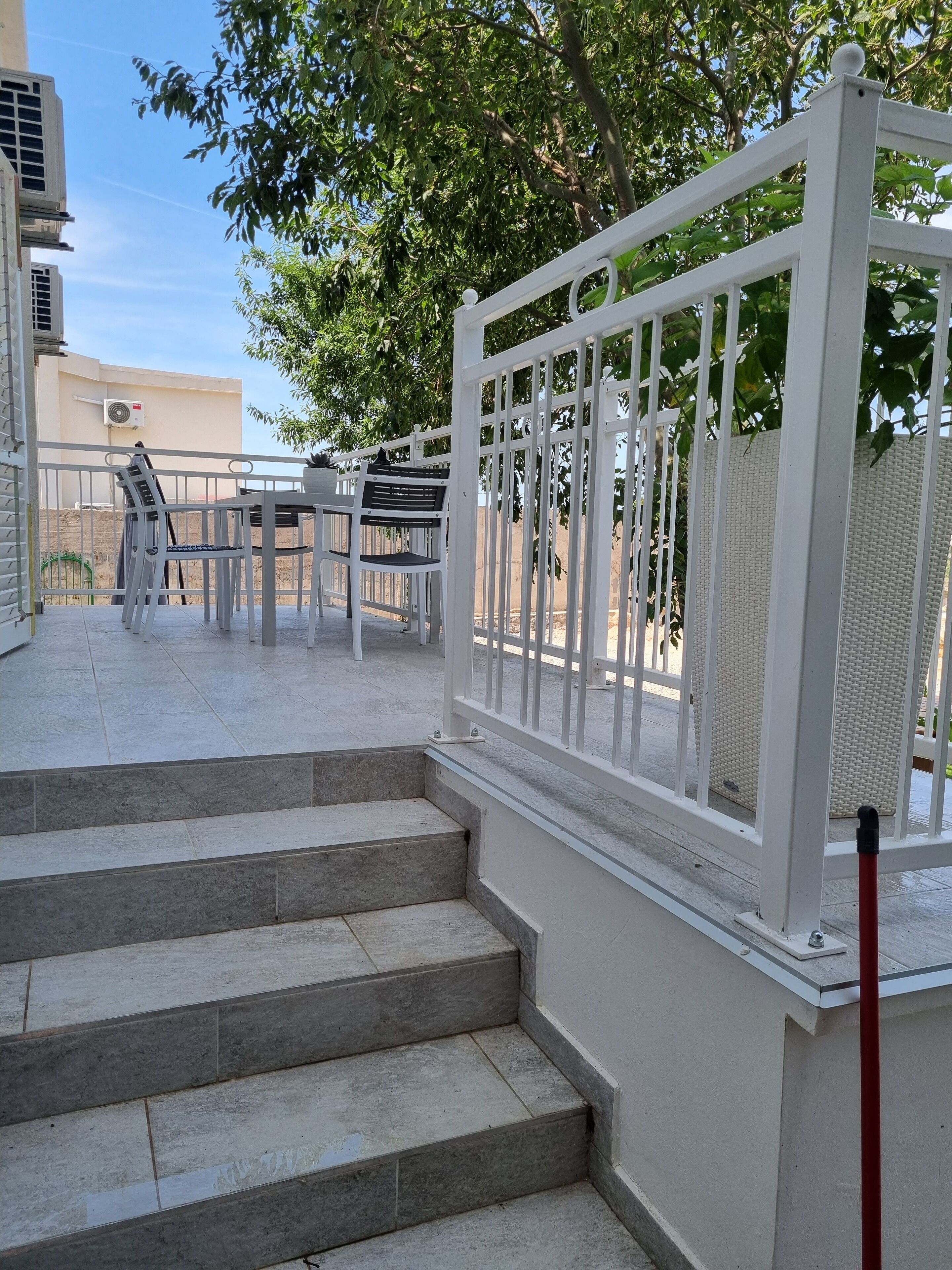 Un escalier extérieur menant à une terrasse agrémentée d’une rambarde en métal blanc, d’une table et de chaises.