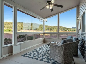 A sunroom with large windows, a ceiling fan, wicker furniture, and a view of a forested landscape. - HOT TUB - WALK TO FOOD, POLAR EXPRESS, DOWNTOWN. CLOSE TO GRAND CANYON!! DOGS OK (Williams)