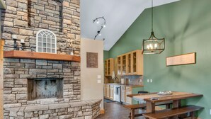 A stone fireplace with a bench, wooden cabinets, and a hanging light fixture in a kitchen area.