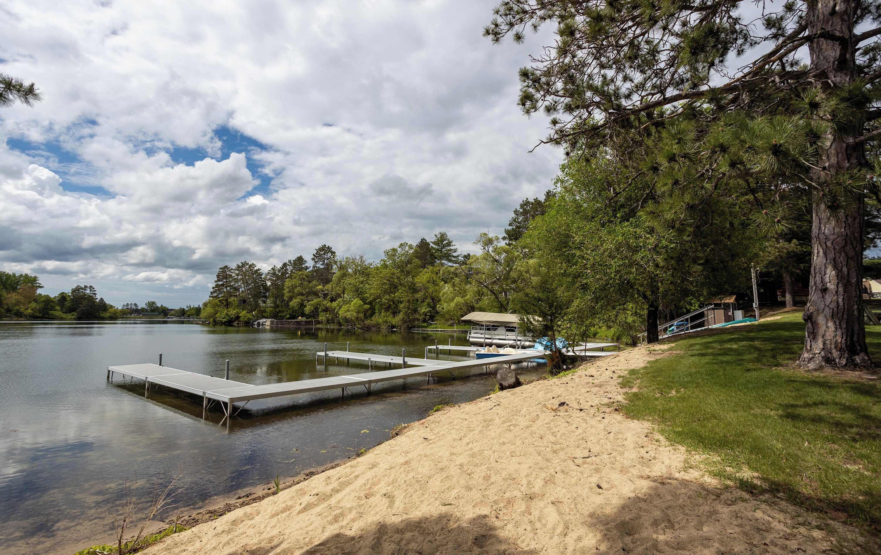 A lakeside dock with a boat, a sandy beach, and a forested area.