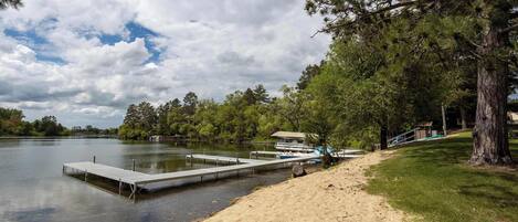 A lakeside dock with a boat, a sandy beach, and a forested area.