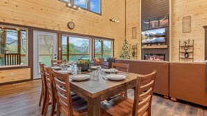 A wooden cabin interior with a dining table set for six, a fireplace, and a Christmas tree. - Hidden Gem Masterpiece By Ghosal Luxury Lodging  (Gatlinburg)
