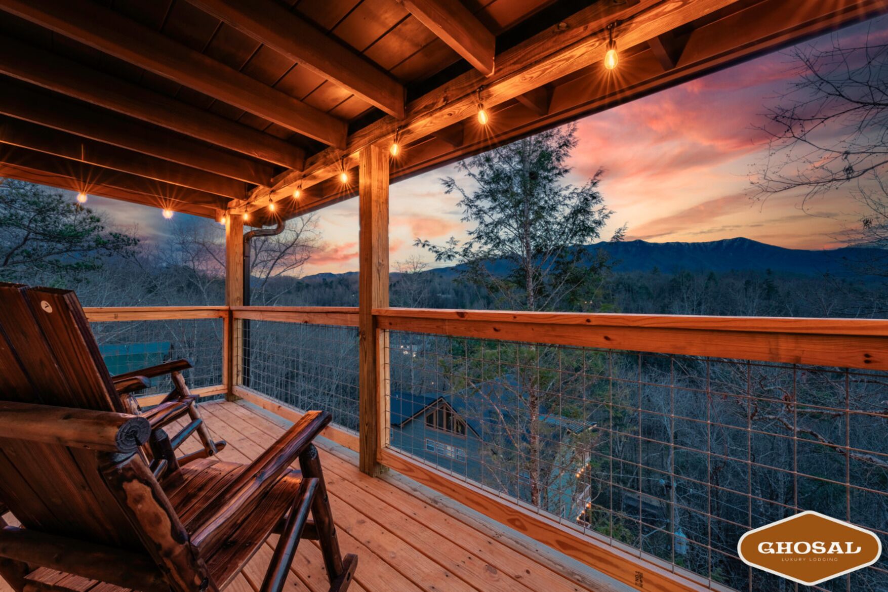 Un ponte di legno con vista sulle montagne e un tramonto. Sono presenti sedie di legno e una ringhiera.