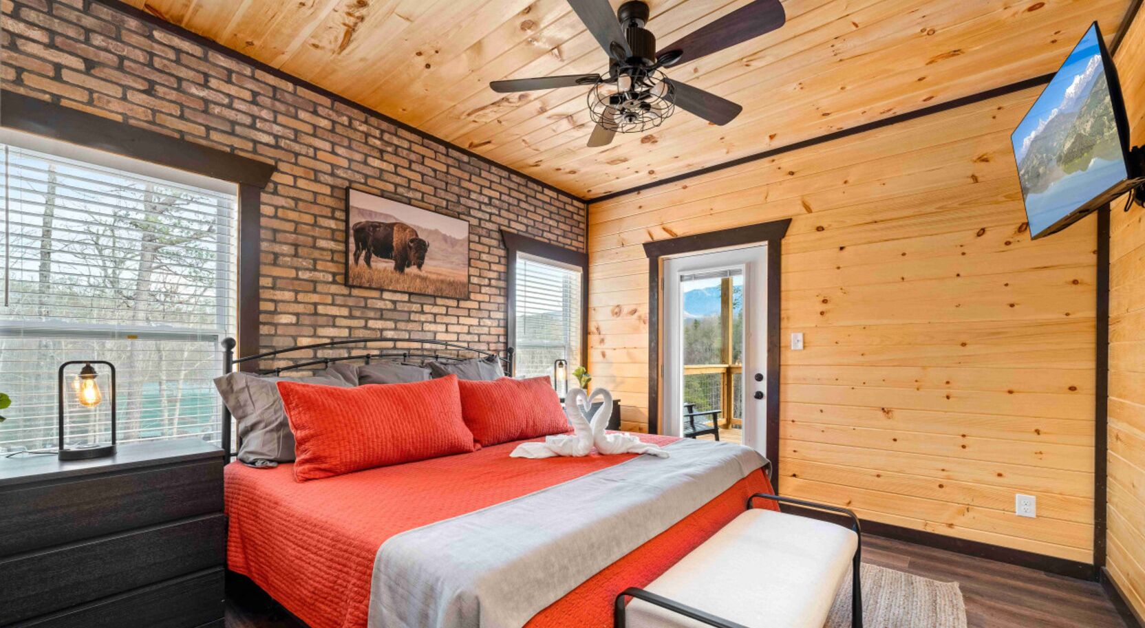 A bedroom with a bed, a ceiling fan, a TV, and a window with blinds.