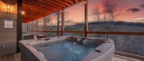 Ein Whirlpool auf einer Holzterrasse mit Blick auf einen Sonnenuntergang über einer Berglandschaft.