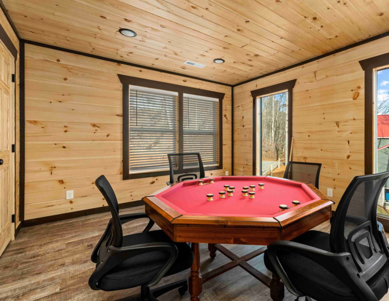 A wooden-paneled room with a pool table, four chairs, and large windows.