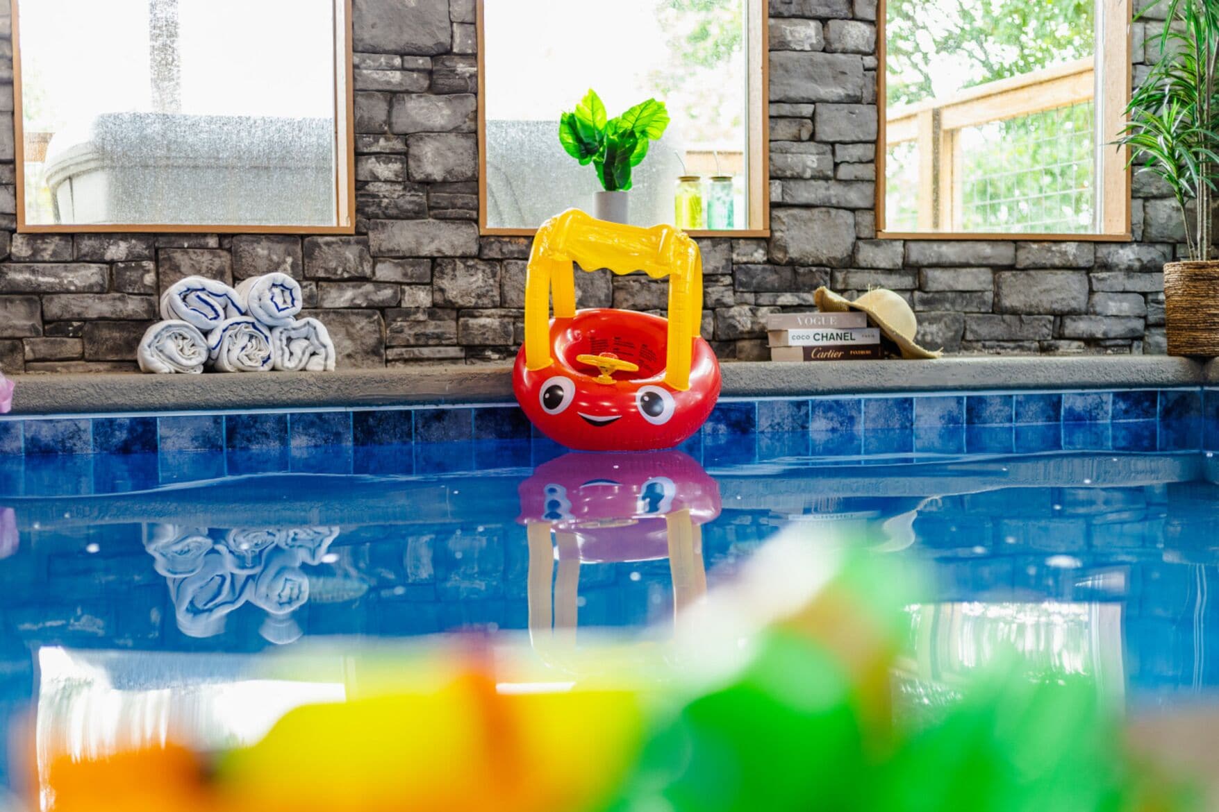 Ein Poolbereich mit einem roten Schwimmreifen, einer Pflanze und Büchern auf einem Regal.