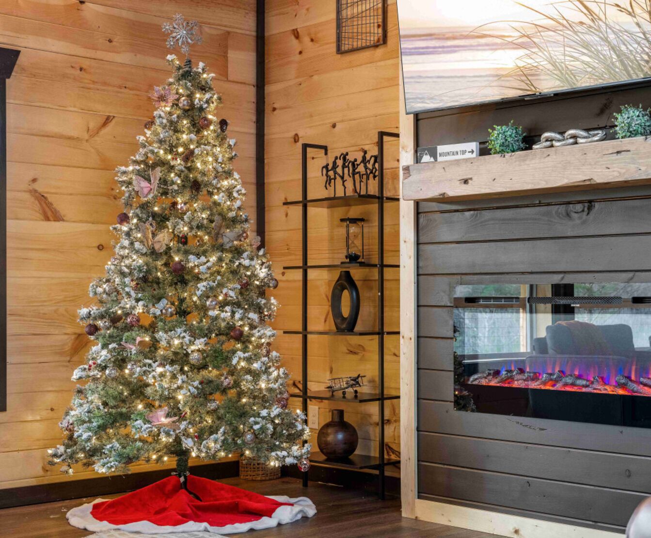 Habitació acollidora amb un arbre de Nadal decorat, una llar de foc i una estanteria amb diversos objectes decoratius.