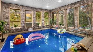 An indoor swimming pool with stone walls and large windows. - Hidden Gem Masterpiece By Ghosal Luxury Lodging  (Gatlinburg)