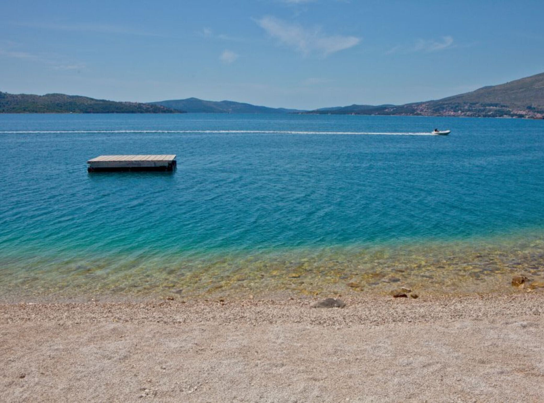 Ein klarer See mit einer Anlegestelle und einem Boot in der Ferne.