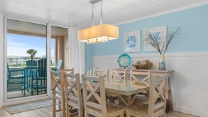 Un coin repas avec une table en verre et des chaises en bois, un luminaire suspendu et des œuvres d’art encadrées accrochées au mur.