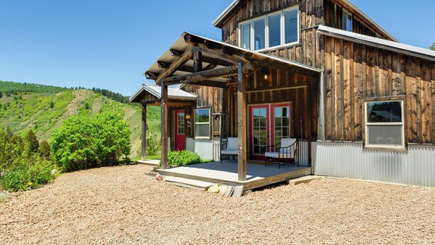 A rustic wooden house with a covered porch, large windows, and a view of a green hillside. - Salt River Access: Mtn-View Star Valley Cabin! (Thayne)